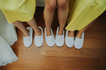 Detail Family feet wearing hotel white slippery during vacation. Bride and bridesmaids slippers detail foot in the makeup room hotel with wooden floor.