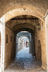 Fototapeta premium Narrow alley (Agiou Fanouriou) with stone arches in the medieval town quarter of Rhodes, Greece.