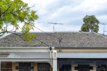 Close-up view of two adjacent Victorian-era suburban houses with roofs covered in weathered slate tiles, cast iron laceworks, and a television antenna on top in Australia.