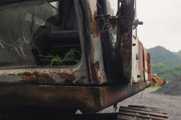 Close up shot of broken glass on the cabin of an excavator in rural Vietnam with plant popping through the window and a rusty metal frame around it