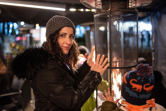Woman and her son warm their hands on the stove on the terrace of a bar in winter