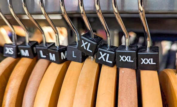 Fashion clothes rack with size tags on wooden hangers of XS, M, L, XL, and XXL different sizing garment tags and labels