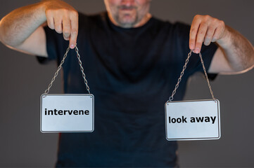 Man holding signs with the words 'intervene' and 'look away'. Symbol for the inner conflict in a...