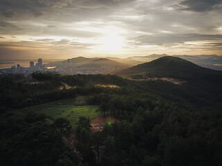 Aerial panoramic shot of the sunset in the mountains overseeing Ha Long, Vietnam. The sunset generates a colorful cloudscape above a forest in Asia