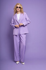 Fashion female model in lilac suit, white shoes, top and sunglasses.