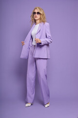 Fashion female model in lilac suit, white shoes, top and sunglasses.