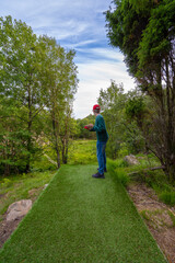 Person throwing a disc at a disc golf course in a forest with a clearing.