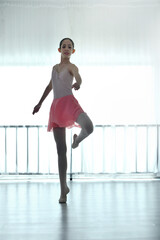 Teenage ballerina practices ballet in a pink outfit in a studio