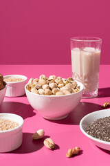 Semillas de chía, sésamo, nueces, pistachos y un vaso de leche vegetal. Frutos secos sobre un fondo rosa