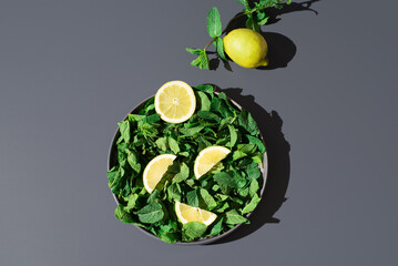 Rodajas de limón y hojas de menta sobre un plato gris sobre fondo gris. Vista superior