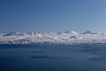 snow capped mountains on lake sevan in clear weather at sunset