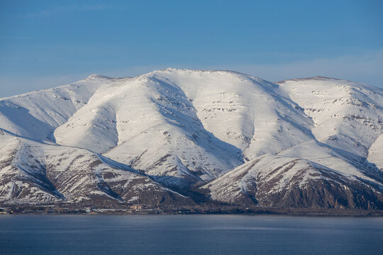 snow capped mountains on lake sevan in clear weather at sunset