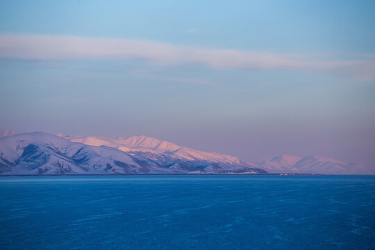 snow capped mountains on lake sevan in clear weather at sunset