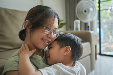 Asian mother and son are hugging. The mother is wearing glasses and the child is wearing a white shirt. Scene is warm and loving