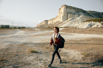 Woman hiking through desert landscape with backpack and mountain in distance