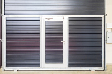 Fototapeta premium Exit from industrial building. Roller shutters with built-in doors. Gate in hangar, view from inside. Doors with closers for roller shutters. Entrance to workshop with possibility of lifting gate