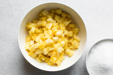 Overhead view of diced pineapple and sugar in white bowls, process of making pineapple cheong or pineapple compote