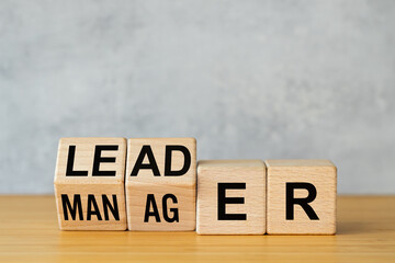 Manager vs leader symbol. Businessman arranged wooden cubes on the table to form the words manager...