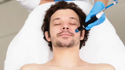 Naklejka premium Facial skin care. A professional female cosmetologist performs a hydraulic procedure on a man in a cosmetology clinic. Vacuum cleaner Hydra. Rejuvenation and hydration