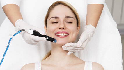 A professional performs a hydropeeling facial treatment on a woman in a modern clinic, focusing on...