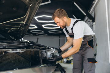 Mechanic Inspecting Car Headlight in Auto Repair Shop with Open Hood