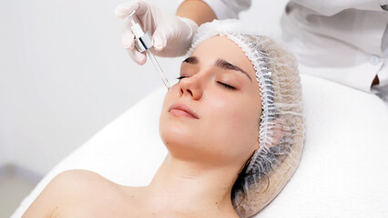 A beautician applies serum to a woman's face using a dropper for even hydration and care. Close-up of a client's face during a spa treatment, perfect for showcasing effective skincare.