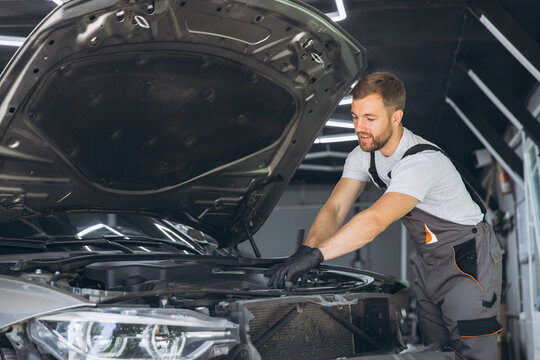 Smiling Auto Mechanic in Overalls Working on Car Engine in Garage