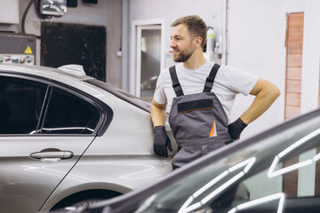 Smiling Auto Mechanic Standing Confidently Beside Silver Car in Garage Workshop