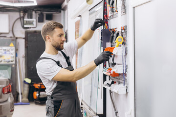 Mechanic in Garage Organizing Tools on Wall Rack in Workshop