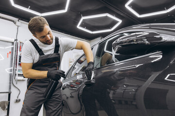 Technician in gloves applies protective film to a car's side door, specialist apply liquid preparations for work preparation.