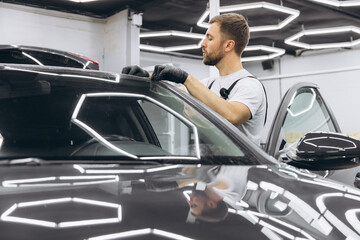 Technician installing protective transparent vinyl film to protect paint and varnish of car, car detailing.