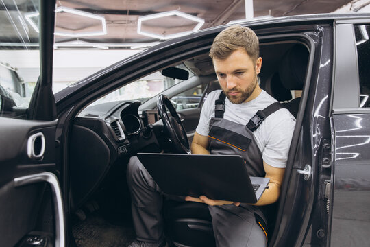 Automotive mechanic running diagnostics software on computer. Mechanic sitting in car and working on laptop while doing vehicle diagnostic test in auto service garage.