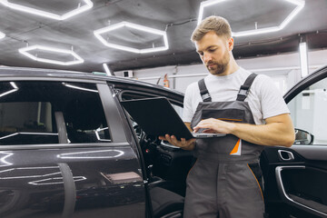 Young professional technician car mechanic man in grey overalls t-shirt use hold laptop pc computer...
