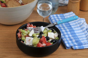 Salade grecque faite maison dans un ramequin noir avec une fourchette servie avec un verre d'eau en gros plan.
