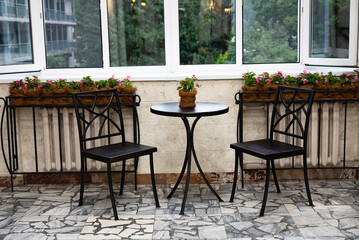 Cozy balcony with table and chairs near window with potted flowers.