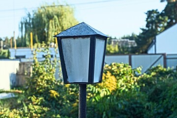 one closed  square old gray with iron black frame electric street decorative retro on rusty pole powerful lantern in green garden in summer daytime