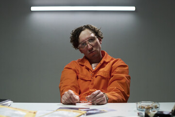 Captured image of a man wearing glasses and an orange jumpsuit holding handcuffs in an indoor...