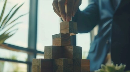 A hand places a wooden block on top of a stack, symbolizing strategy, growth, and balance in a sunlit room.