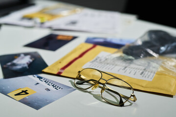Close-up of eyeglasses, evidence photographs, and documents laid out on a desk used for an investigative analysis during law enforcement activity