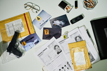 Collection of crime scene evidence on an office desk includes photographs, cigarette butts,...