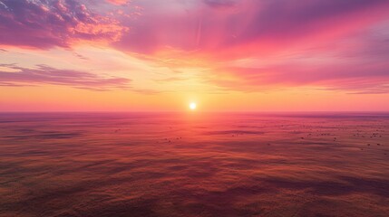 Obraz premium A panoramic view of the Serengeti at sunrise, with the vast plains stretching out under a pink and orange sky.