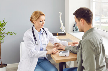 Fototapeta premium Caring female professional clinic doctor examining patient, measuring arterial blood pressure using medical tonometer during hospital regular checkup appointment visit, health examination, cardiology
