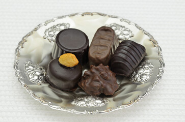 Different kinds of chocolate pralines on a silver plate, close up, isolated on white background