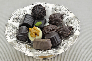 Different kinds of chocolate pralines on a silver plate, close up, isolated on white background