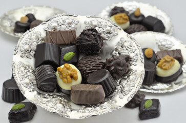 Different kinds of chocolate pralines on silver plates, close up, isolated on white background