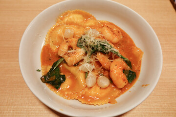 close up of Italian lobster sauce prawns shrimp stuffed ravioli with herbs on a white bowl