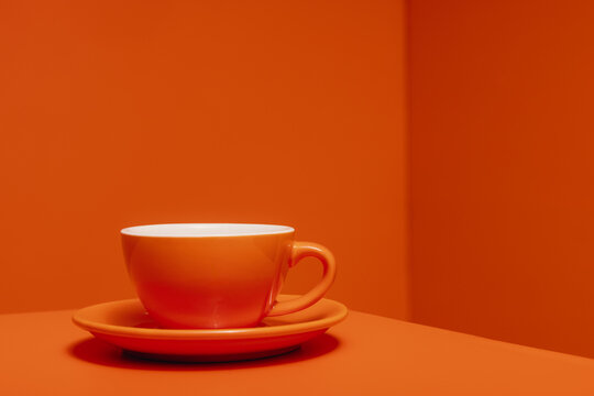 Monochromatic studio shot of an orange cup and saucer on solid colored background