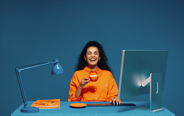 Employee enjoying a coffee break while working at her computer, color blocking studio shot