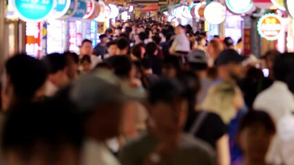 Defocused view of bustling narrow alley, traditional street food market at Busan, in night time. Popular place crowded with tourists and locals exploring various vendors selling seafood and snacks.