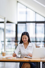 Obraz premium Asian Businesswoman Using laptop computer and working at office with calculator document on desk, doing planning analyzing the financial report, business plan investment, finance analysis concept. 